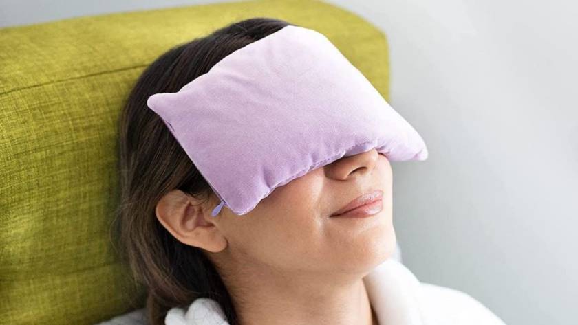 The image shows a woman using an eye pillow for relaxation.